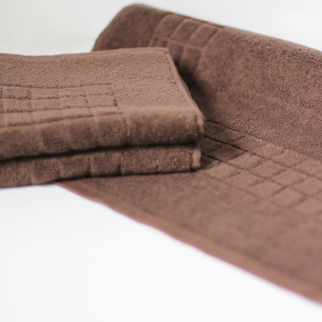 A set of brown textured towels, including a folded stack of hand towels and a larger bath mat, displayed on a clean white background.