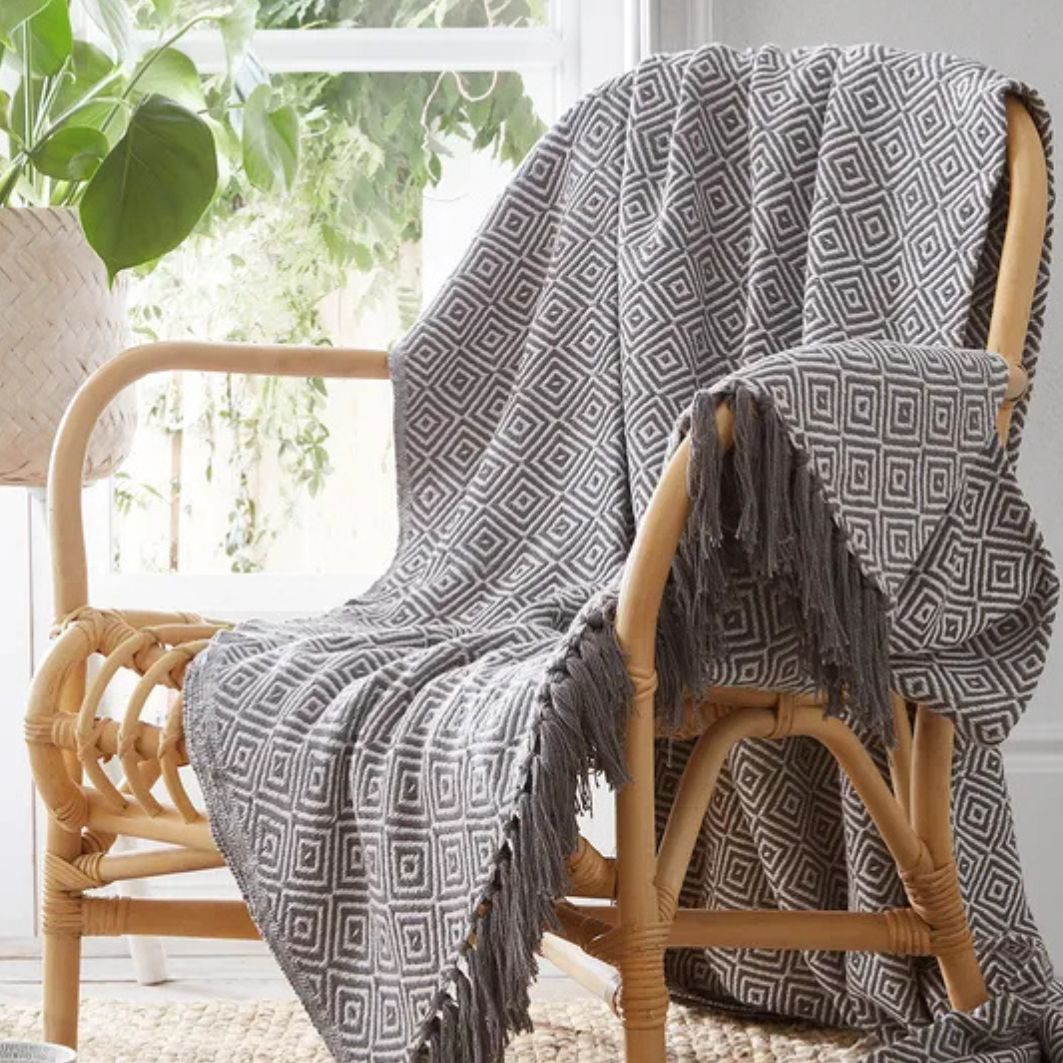 Charcoal patterned throw blanket draped over a wicker chair in a bright room with plants.