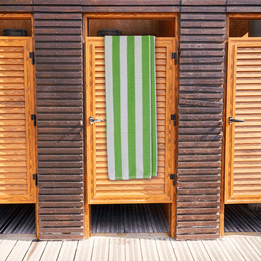 Wooden beach hut with a bright green and white striped towel hanging on the door.
