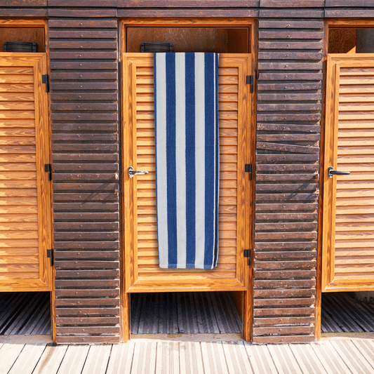 Striped navy and white, budget-friendly beach towel hanging on a wooden door of a beach hut