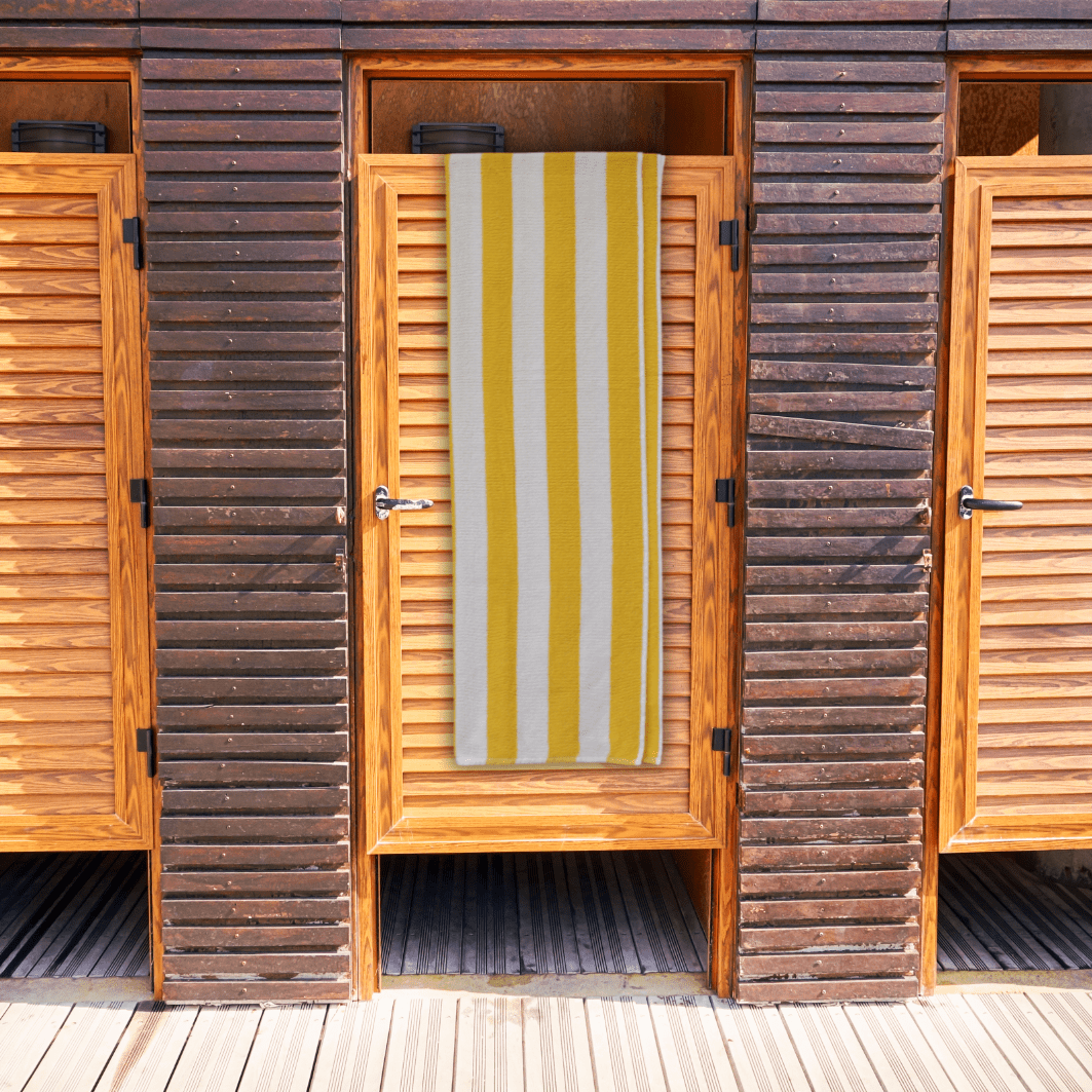 Wooden beach hut with a yellow and white striped towel hanging on the door
