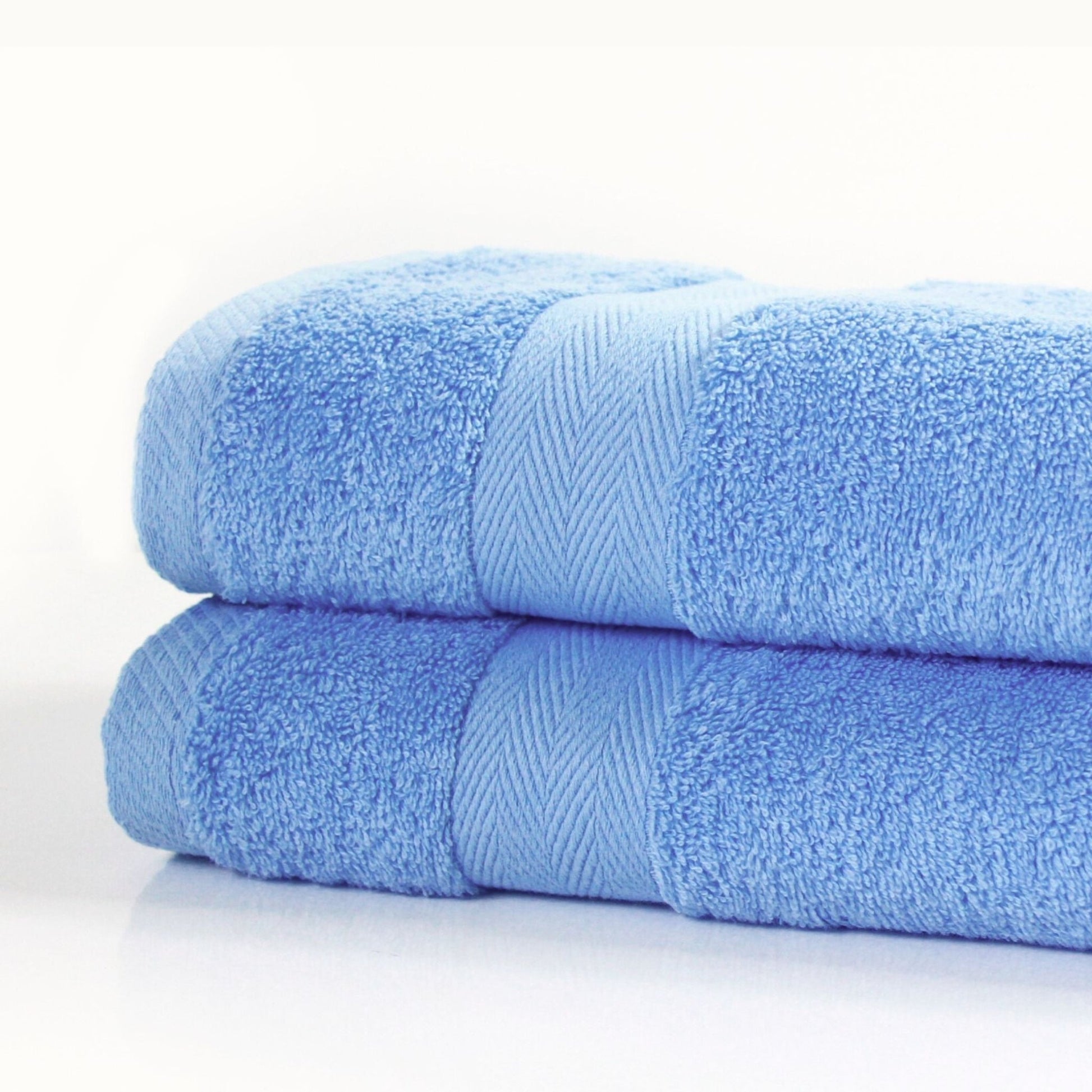 Two 600 gsm luxury cotton bath towels in blue, stacked on a white background