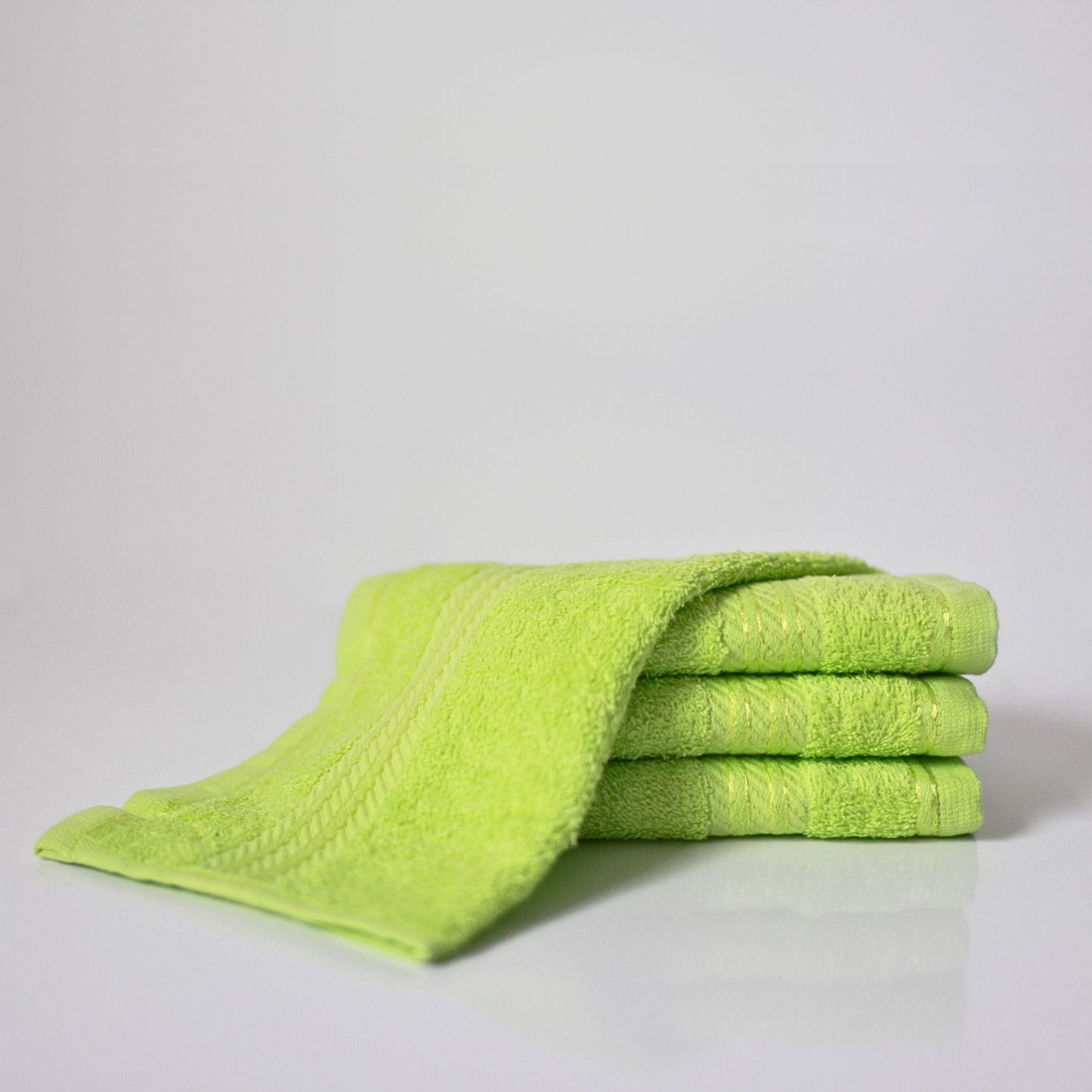 Stack of 500gsm lime green cotton hand towels on a light grey background 