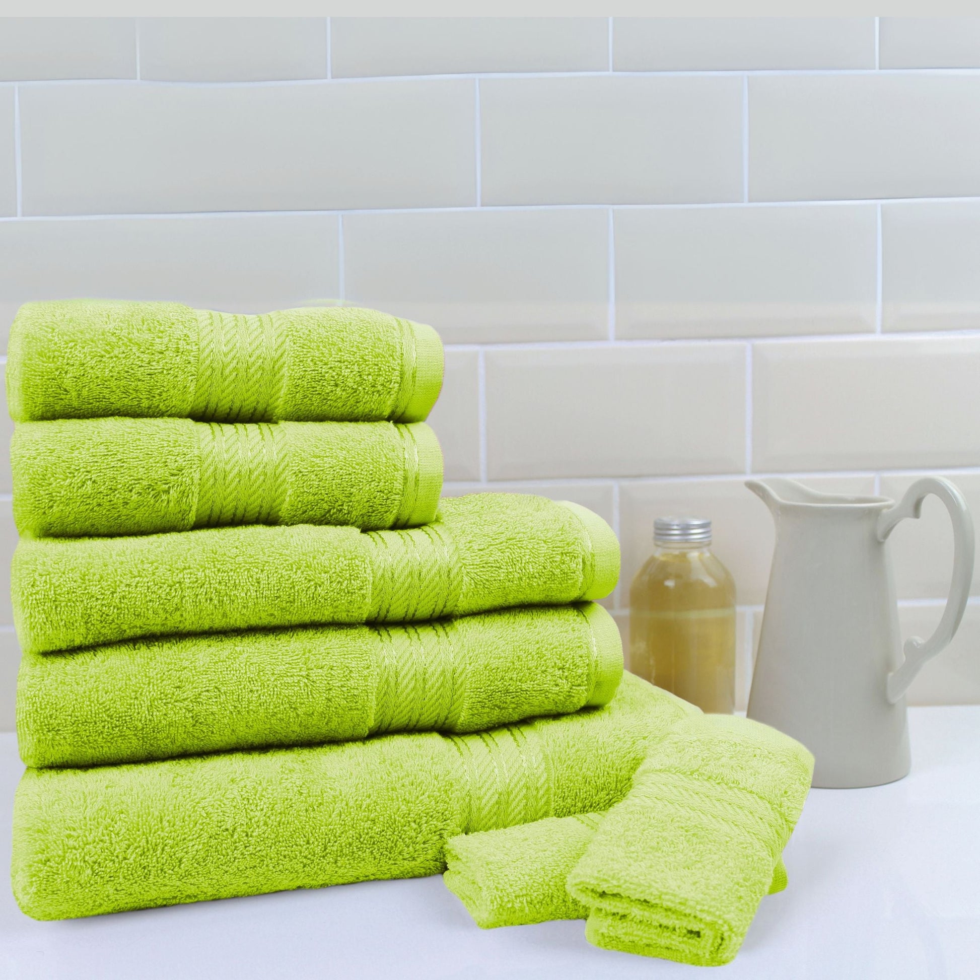 Stack of 500 gsm lime green cotton bath towels on a white surface with a tiled wall background