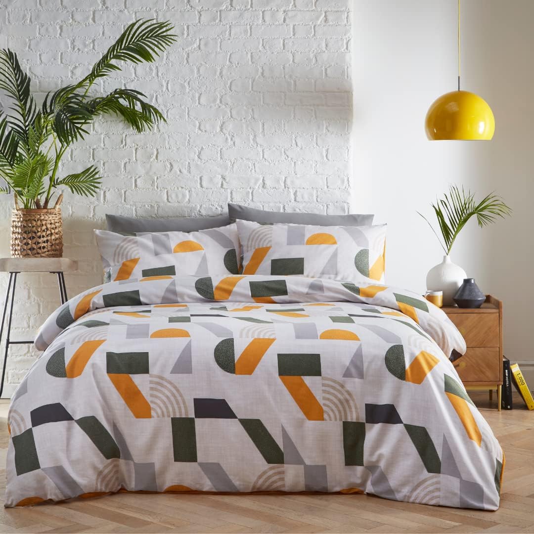 A bed dressed in a white duvet cover and matching pillowcases featuring a modern geometric pattern of orange, olive green, and gray curved and angular shapes, styled in a bright bedroom with a white brick wall, wooden nightstand, and yellow pendant light.