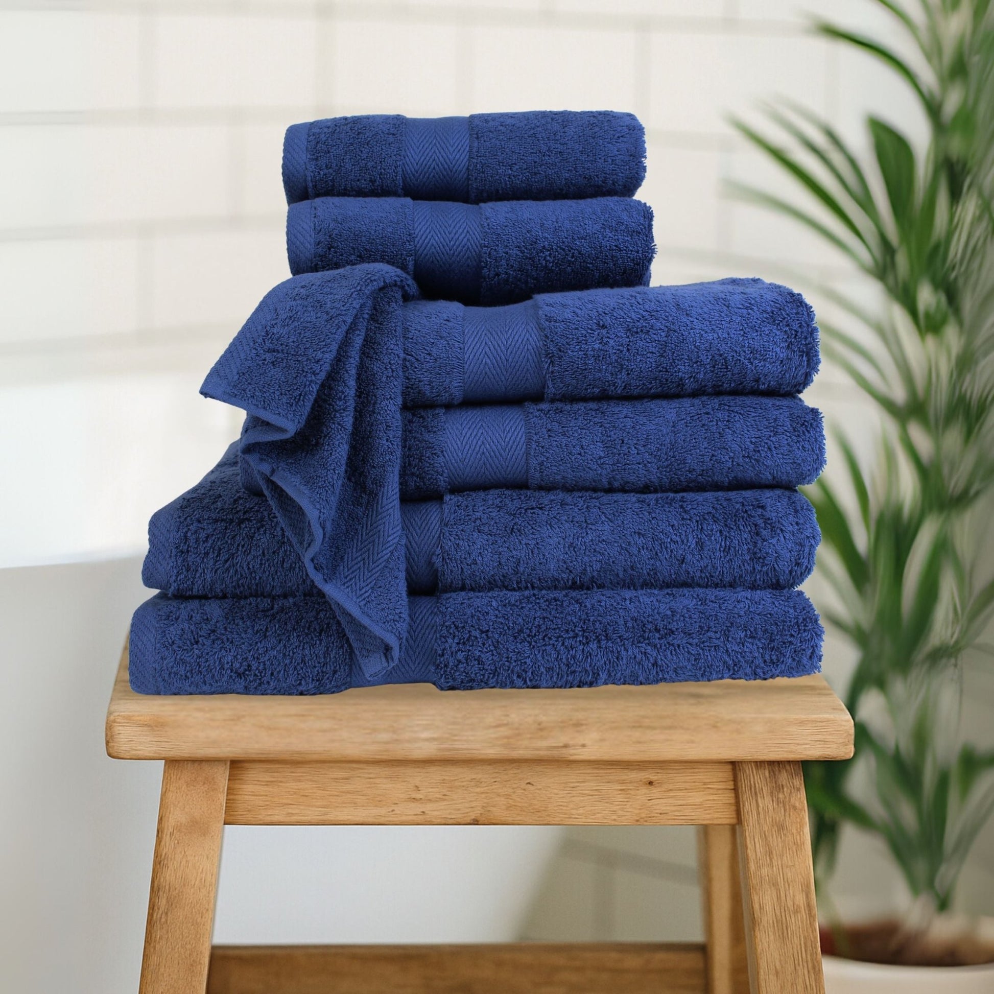 Stack of luxury bath towels in Navy Blue, made from fine combed cotton with thick 600 GSM pile in bathroom setting.