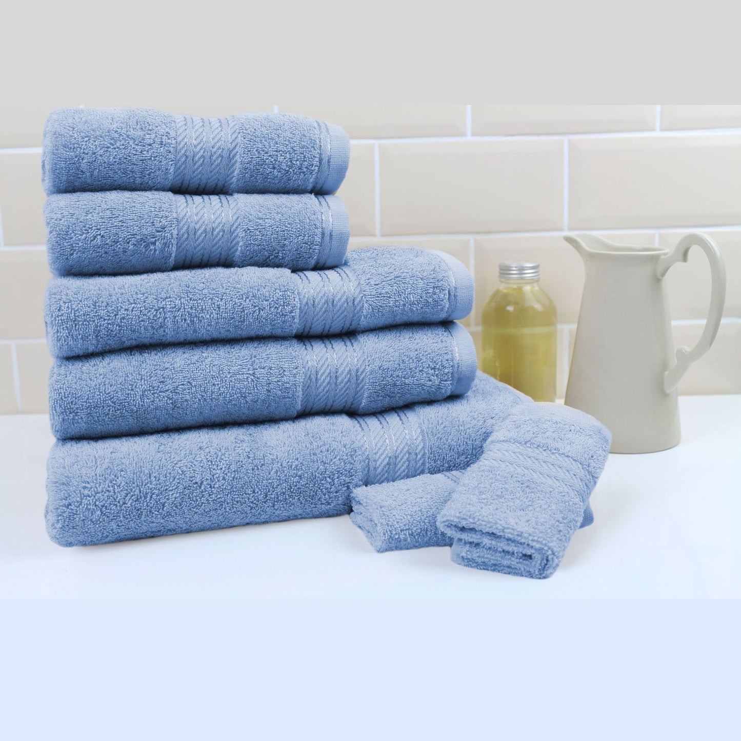 Stack of blue bath towels on a white surface with a tiled wall background