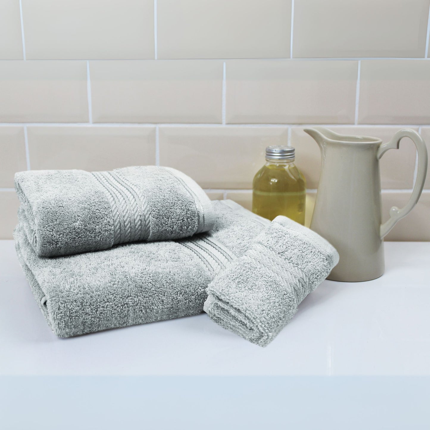 Stack of grey towels on a white surface with a tiled wall background
