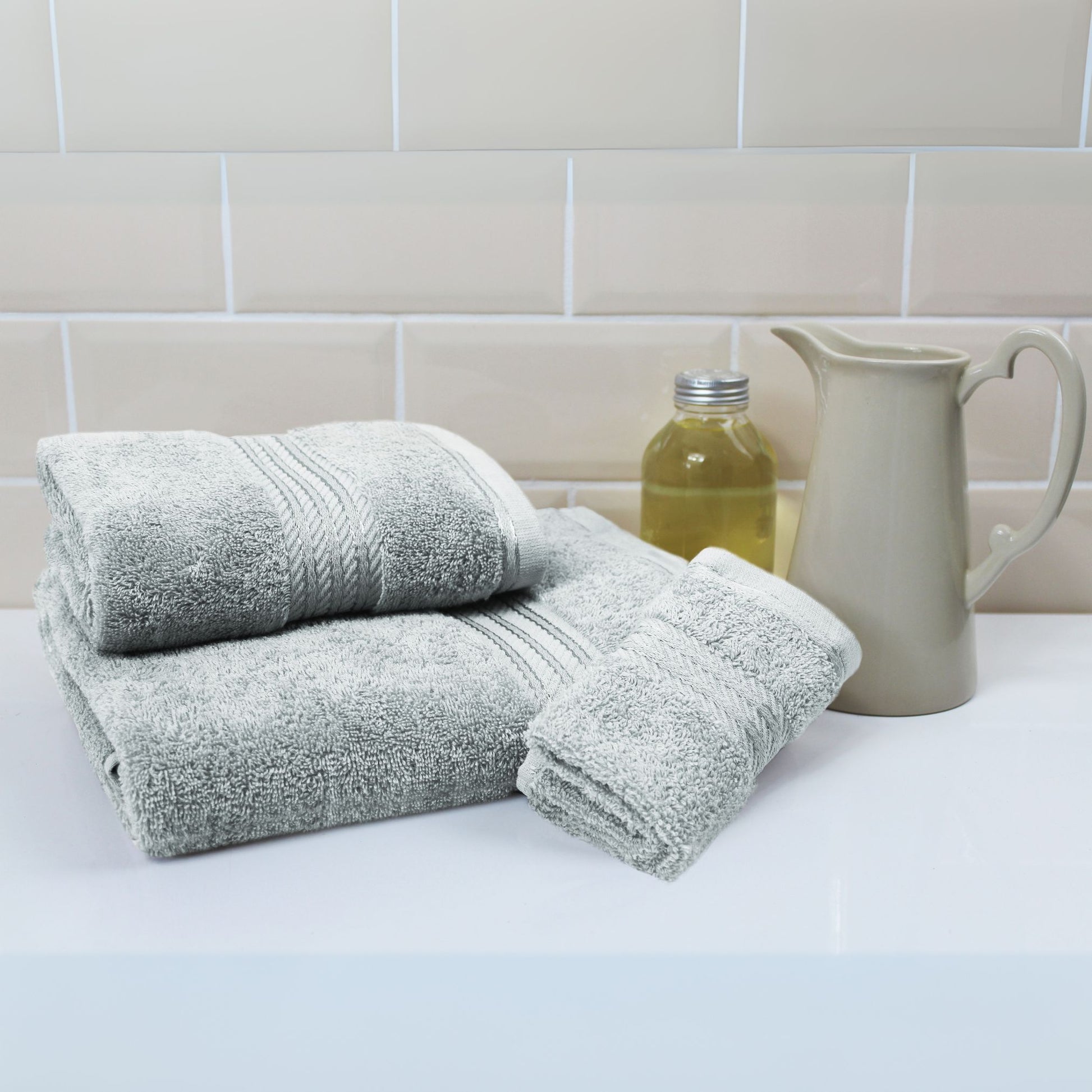Stack of grey towels on a white surface with a tiled wall background