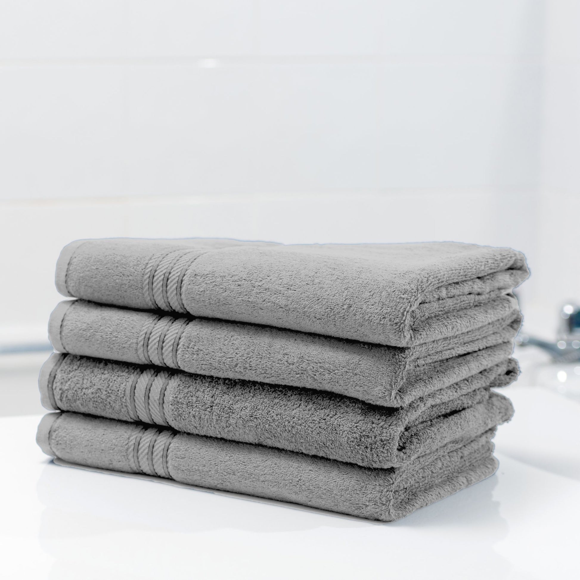 Stack of grey bathroom towels on a white surface with a neutral background