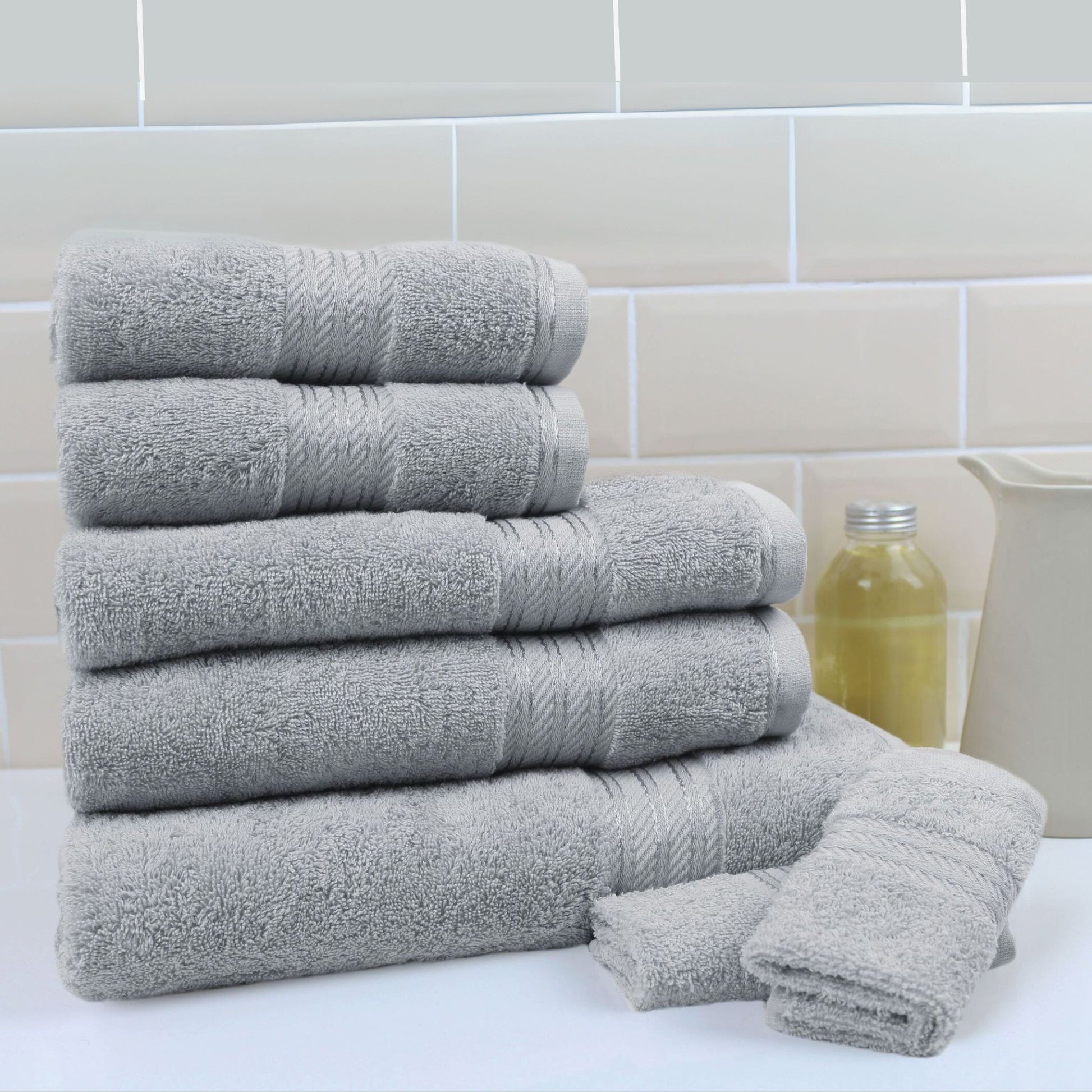 Stack of grey bathroom towels on a white surface with a tiled wall background