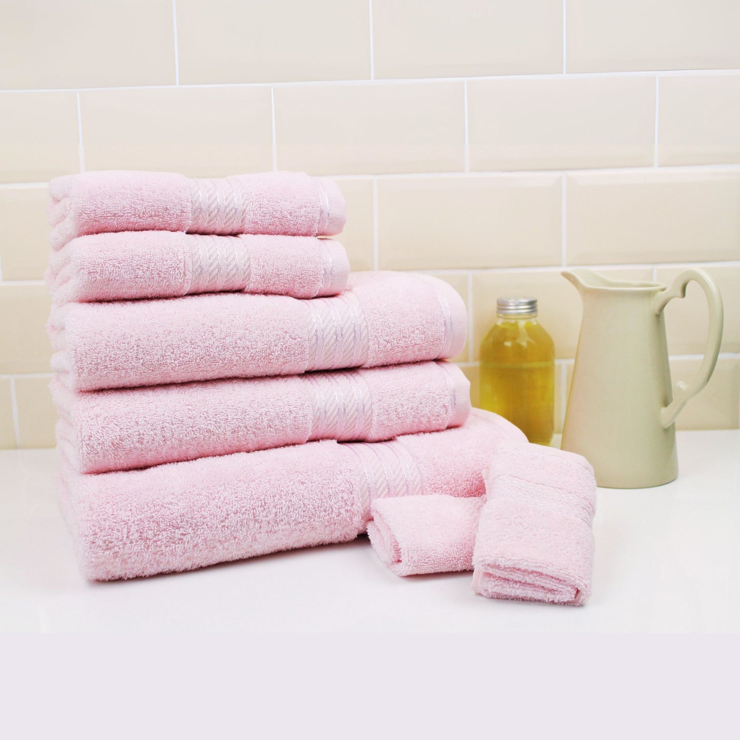 Stack of pale pink bath towels on a bathroom counter with a tiled wall background
