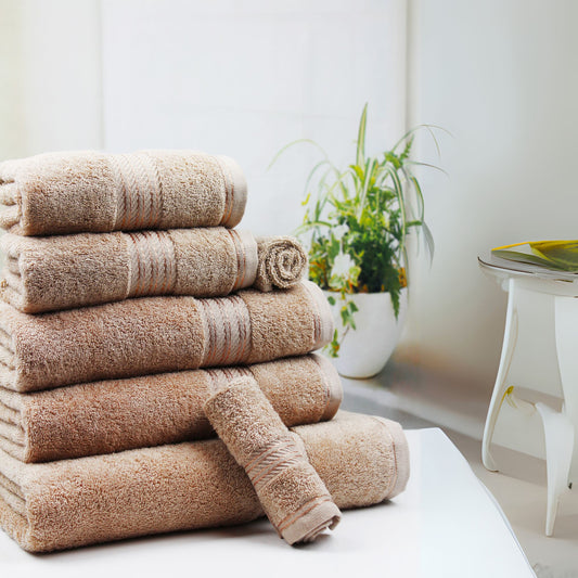 Stack of beige bathroom towels on a white surface with a plant in the background