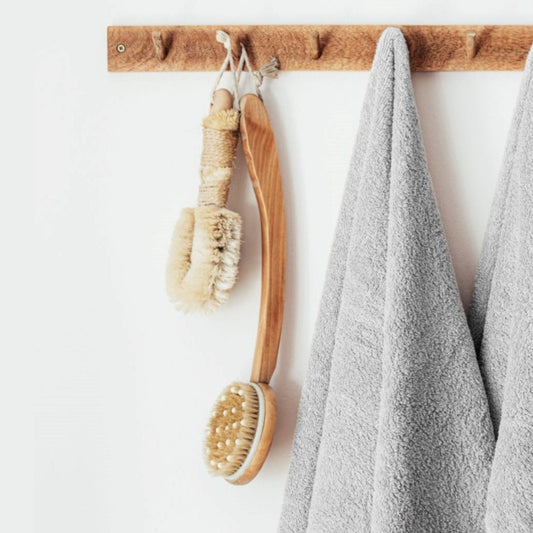 Wooden bath brush and scrubber with a grey cotton bathroom towel hanging on a wooden rack.