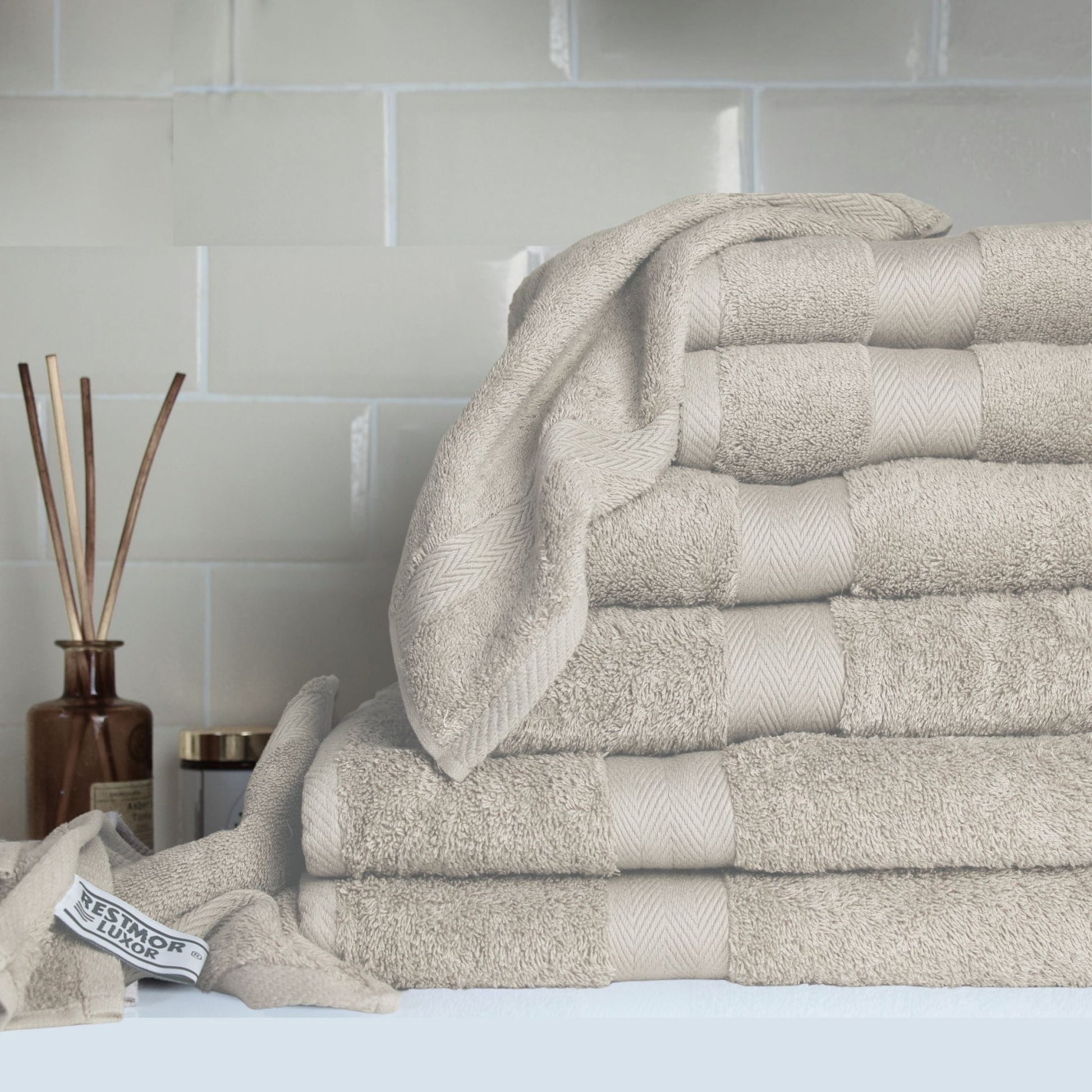 Stack of stone coloured premium bathroom towels made from fine combed cotton with 600 GSM pile, in a luxury bathroom setting