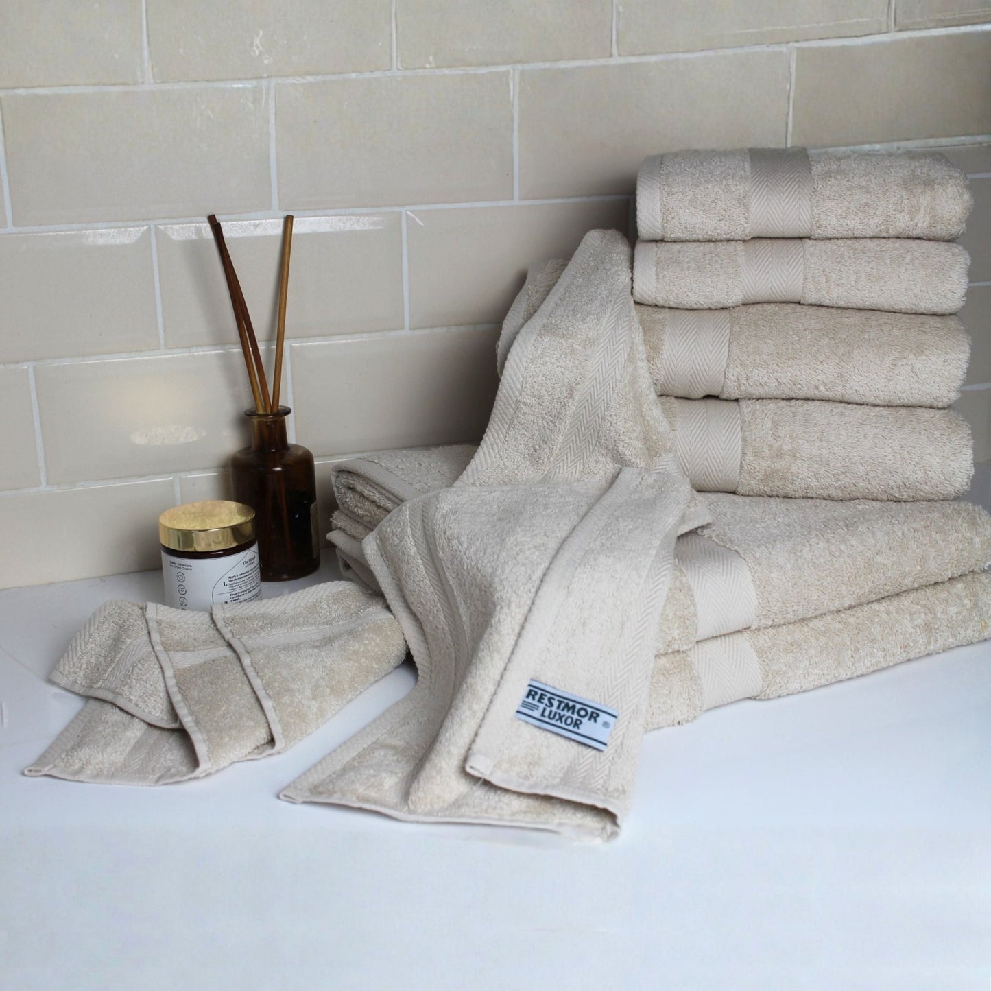Stack of natural stone coloured bath towels made from fine combed cotton with 600 GSM pile displayed on a luxury bathroom background