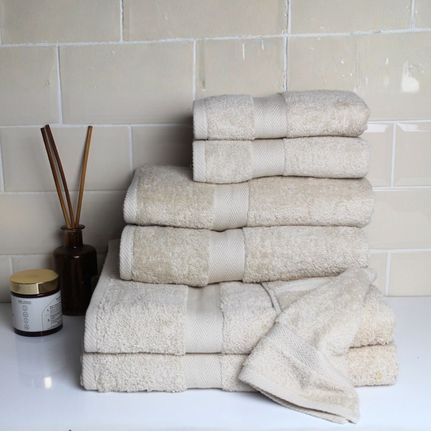 Stack of natural stone coloured premium bathroom towels in fine combed cotton with a 600 GSM pile, displayed in a luxury bathroom scene 