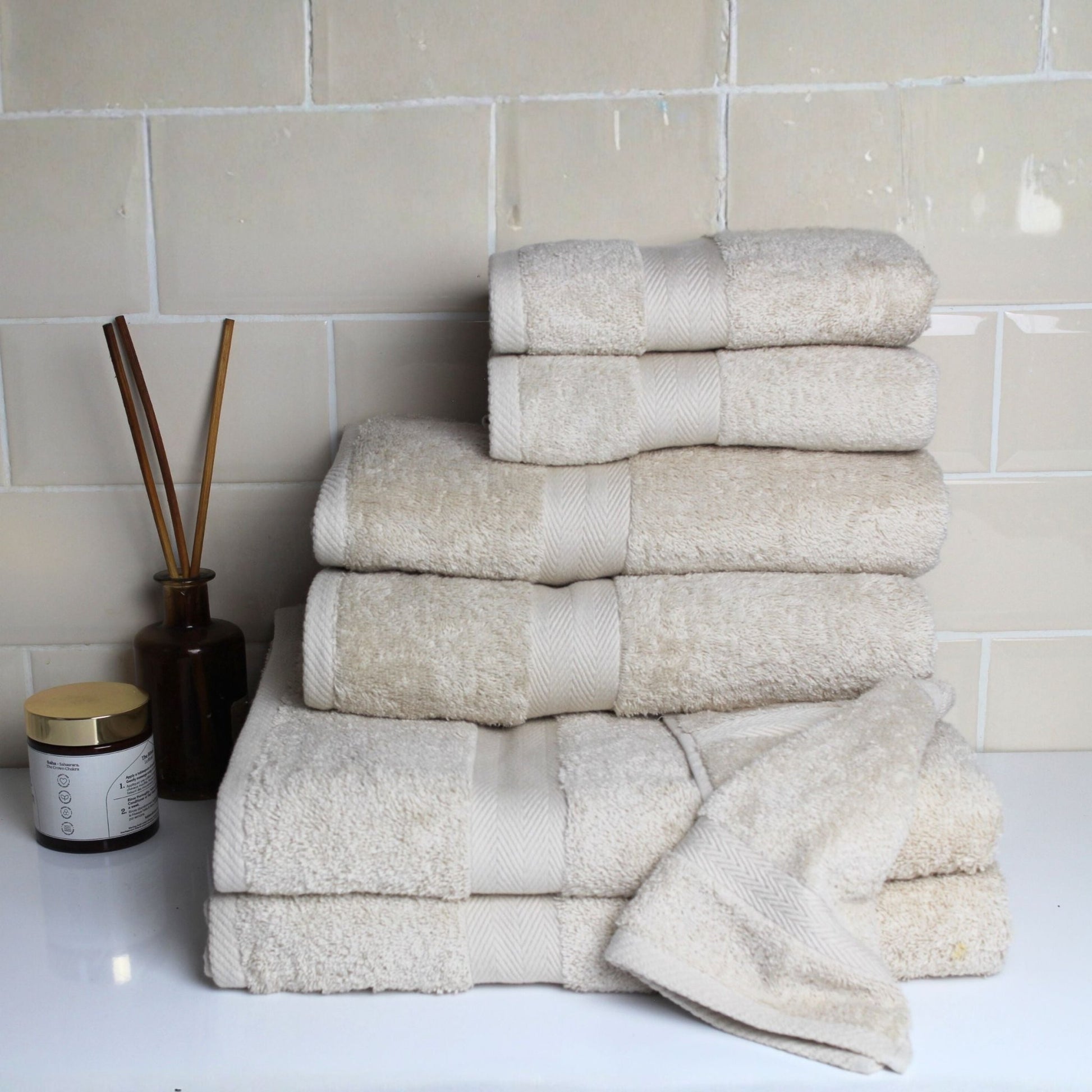 Stack of natural stone coloured premium bathroom towels in fine combed cotton with a 600 GSM pile, displayed in a luxury bathroom scene 